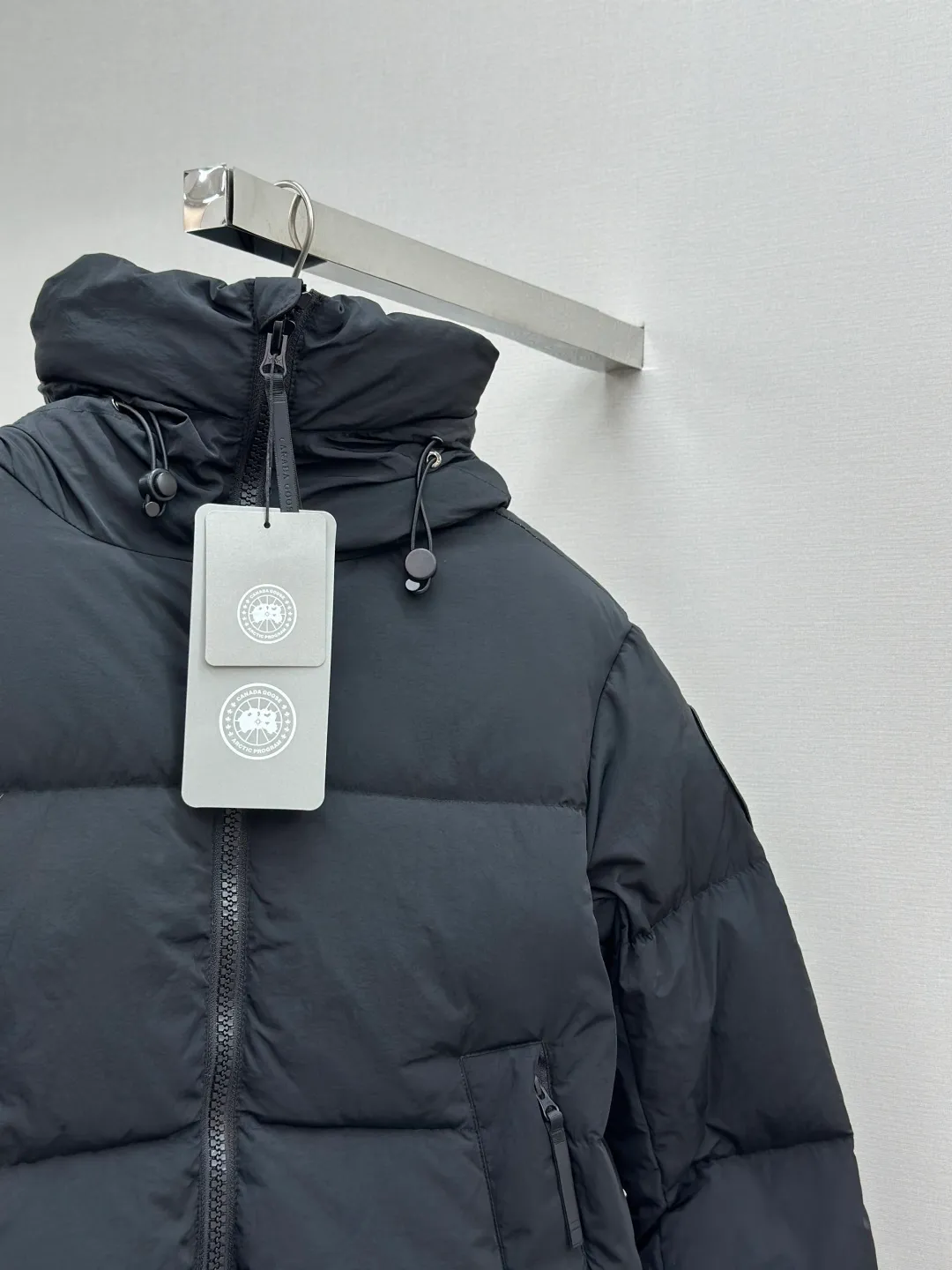 P1010 Canada Goose Black Label Badge Hooded Down Jacket (khaki) The high-quality filling is made of 90 national standard high-quality white duck down, selected high-loft velvet, weighing 240g, light and warm, with excellent temperature locking performance and good resilience. The fabric is woven with 400T high-count yarn. After special water-repellent treatment, the surface forms a lotus leaf effect - raindrops will slide down like beads, and snow particles will fall off when touched. The tear resistance reaches 200N (approximately 20kg load-bearing), the light gray matte texture breaks the stereotype of "outdoor clothing = hardcore", and the soft luster presents a high-end matte effect under urban neon lights, seamlessly switching scenes from ski resorts to CBD office buildings. The ribbon is woven with polyester as the base, and the brand letters are decorated on the ribbon through high-precision computer embroidery. The edges of the pattern are clear, the stitches are fine and even, and multiple layers of embroidery thread are stacked to enhance the three-dimensional effect. Precision thread reinforcement prevents linting and ensures the fluffy and resilient elasticity lasts as new. The embedded cuffs are three-dimensionally woven to form a "wavy" elastic structure, which forms natural folds when fitting the wrist, increasing the contact area with the skin, thus improving the windproof effect. At the same time, micro-velvet treatment is added to the inside of the cuffs, which feels like a second layer of skin and avoids friction on the skin from metal zippers or hard fabrics. Size:S-M-L-XL